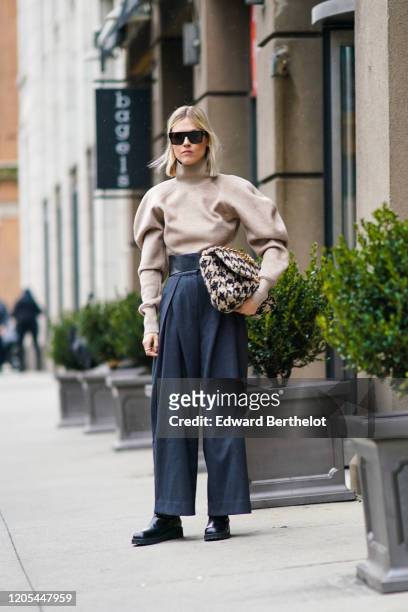 Linda Tol wears sunglasses, a gray turtleneck pullover with puff sleeves, a black and white houndstooth pattern tweed bag, dark pants, black leather...
