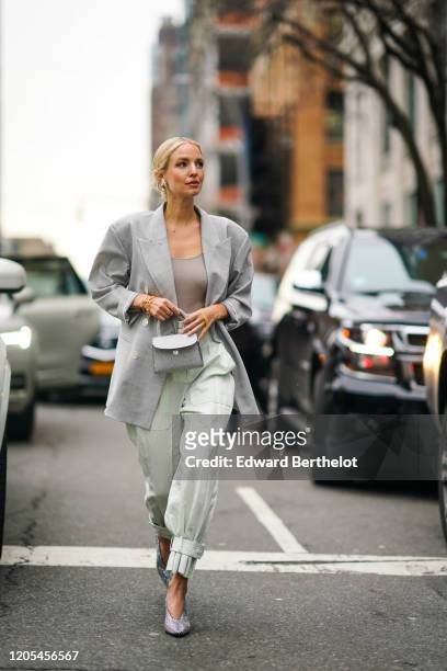 Leonie Hanne wears a gray oversized blazer jacket, a mini bag, pale green flowing pants, pointy shoes, a low neck gray top, during New York Fashion...