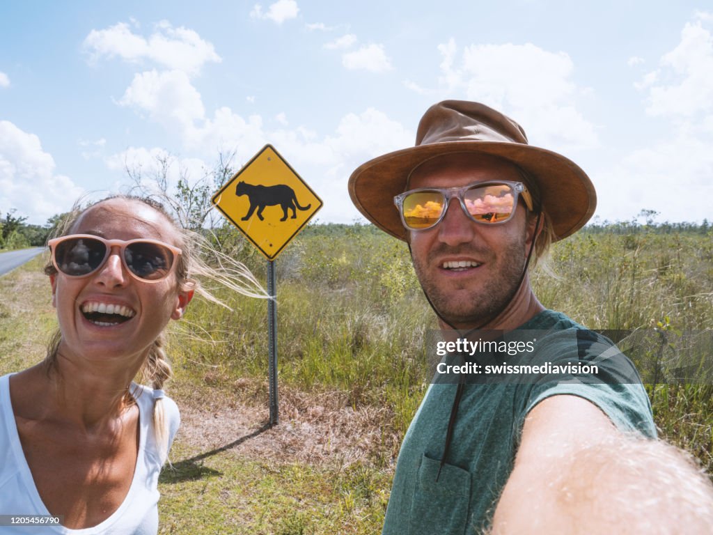 Young couple taking selfie on empty highway road near Florida Panther warning sign
