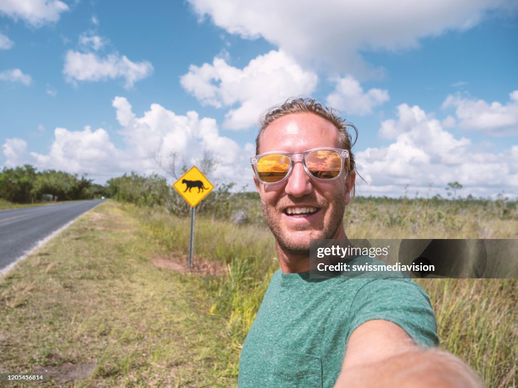 Young man taking selfie on empty highway road near Florida Panther warning sign