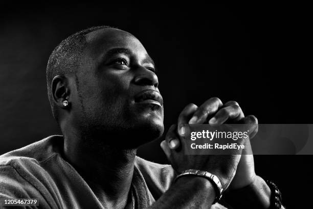 devout african or african american man prays, hands clasped - low key imagens e fotografias de stock