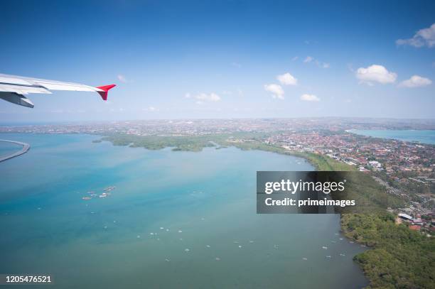 tropical island coastline view from the plane island sneak peaking through the clouds seen from a plane's window bali ,indonesia - summit takes place in singapore stock pictures, royalty-free photos & images