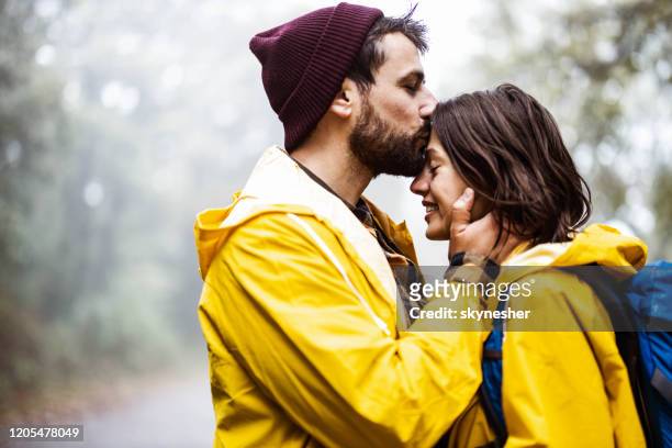 gelukkig hartelijk paar in regenjassen die in aard genieten. - couples kissing shower stockfoto's en -beelden