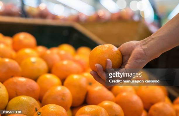 man chooses oranges in the supermarket. - tangerine stock pictures, royalty-free photos & images