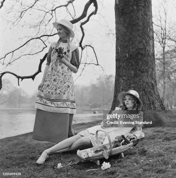 Two female fashion models wear summer cotton midi and mini dresses with straw hats beside a lake in a park, 12th April 1971.