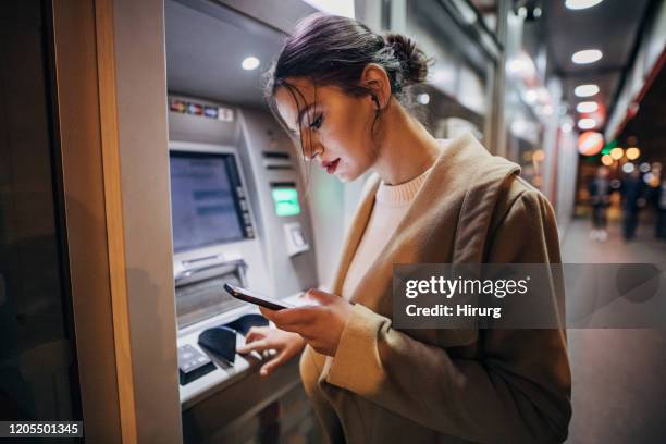 young teenage girl using atm machine and smart phone - atm cash stock pictures, royalty-free photos & images