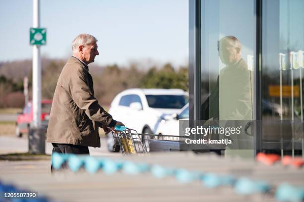 senior man entering supermarket with shopping cart - entering shop stock pictures, royalty-free photos & images