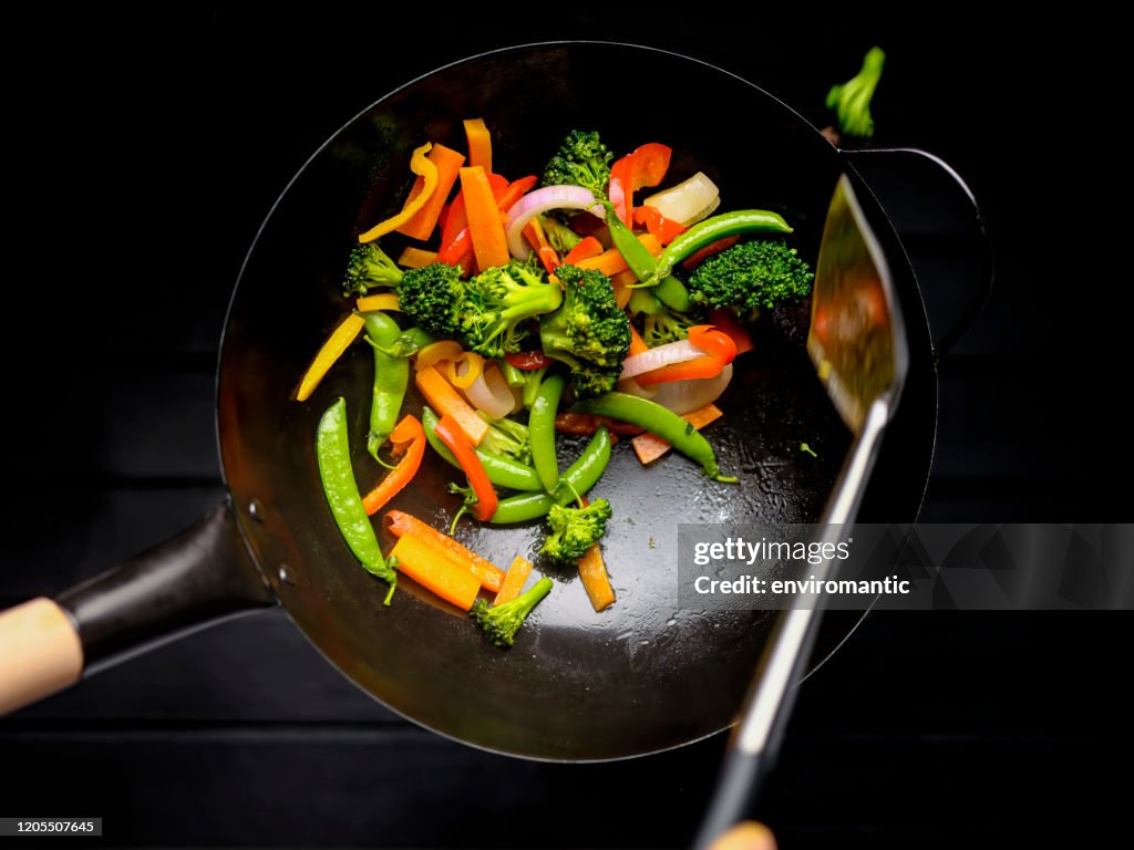 Rühren Braten und sauteing eine Vielzahl von frischen bunten Markt Gemüse in einem heißen Wok.