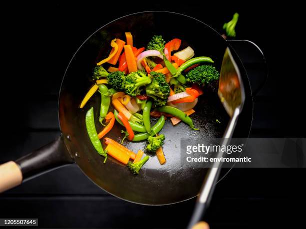 stir frying and sauteing a variety of fresh colorful market vegetables in a hot wok. - salteado imagens e fotografias de stock