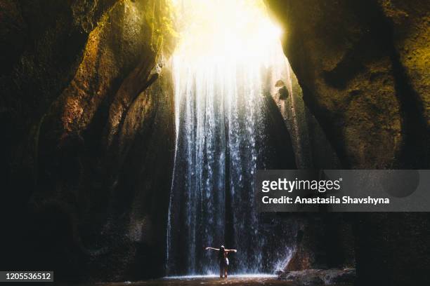 frau trifft sonnenaufgang in der höhle unter dem großen wasserfall auf bali insel, indonesien - wasserfall stock-fotos und bilder