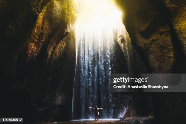 mujer se encuentra con el amanecer en la cueva bajo la gran cascada en la isla de bali, indonesia - catarata fotografías e imágenes de stock