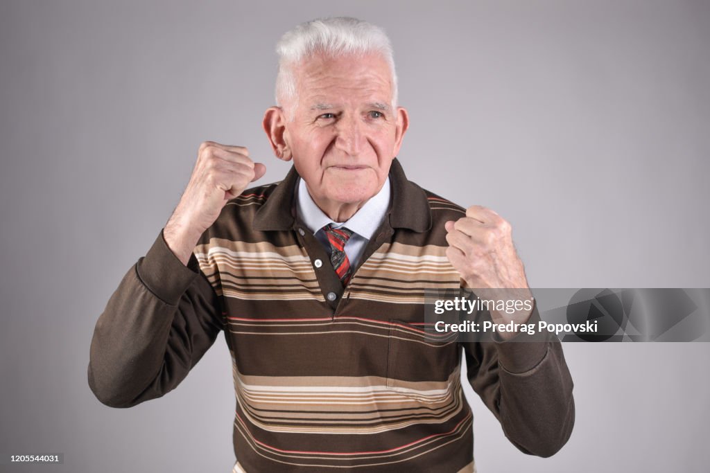 Healthy , happy senior man punching on studio background