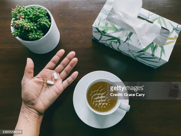woman's hand holds pills above wood table - paracetamol stockfoto's en -beelden