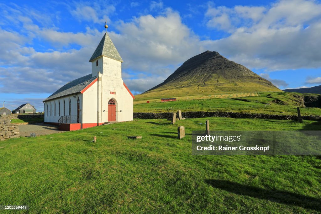 A church with cemetery on a meadow wit a pyramidal mountain is in the background
