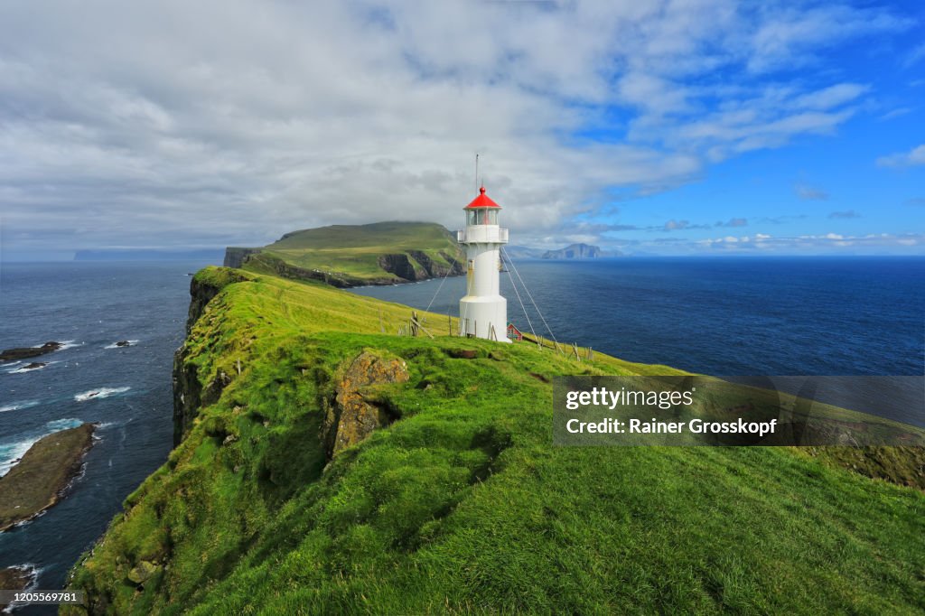 A small white lighthouse wit a red roof on top of grassy cliffs of Mykines Island
