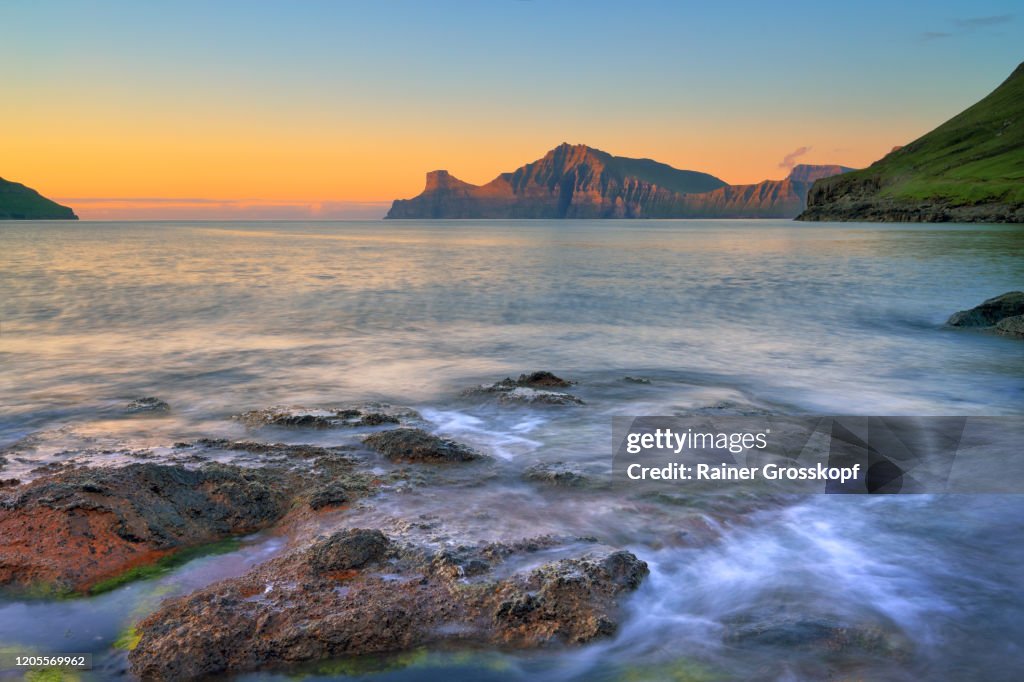 View over a rocky shore at steep and rocky mountains illuminated by the setting sun