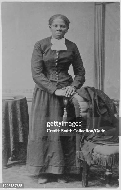 American abolitionist and political activist Harriet Tubman looking directly at the camera with folded hands resting on the back of an upholstered...