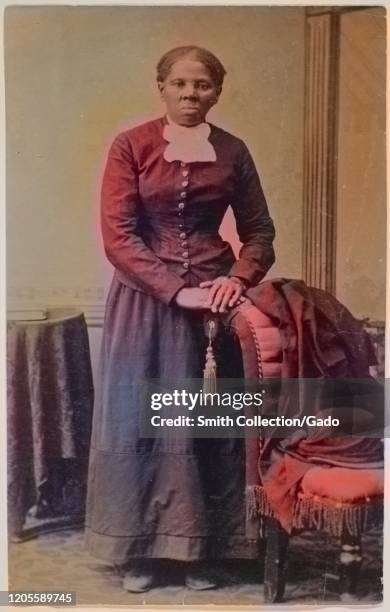 Full length portrait of activist Harriet Tubman looking directly at the camera with folded hands resting on back of an upholstered chair, 1871....