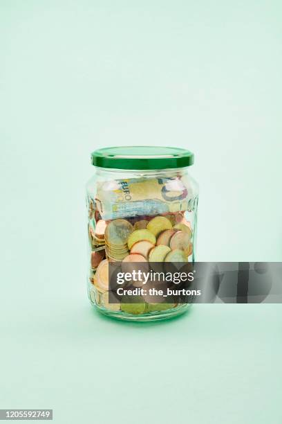 jar filled with euro coins and banknotes on turquoise background - european union coin stock pictures, royalty-free photos & images