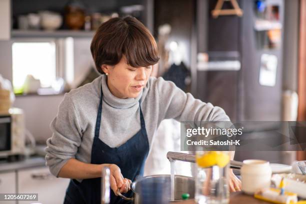 donna che versa acqua alla pentola in cucina domestica - casalinga foto e immagini stock