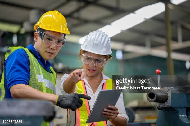 afro woman engineer and mechanical technical in overalls using digital tablet and discuss to each other during their working in the factory. - funktionskleidung stock-fotos und bilder