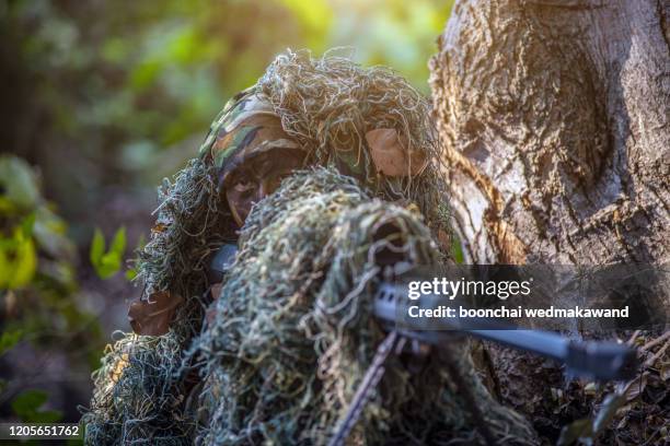 sniper laying on the grass looking through scope at the target - scharfschütze stock-fotos und bilder