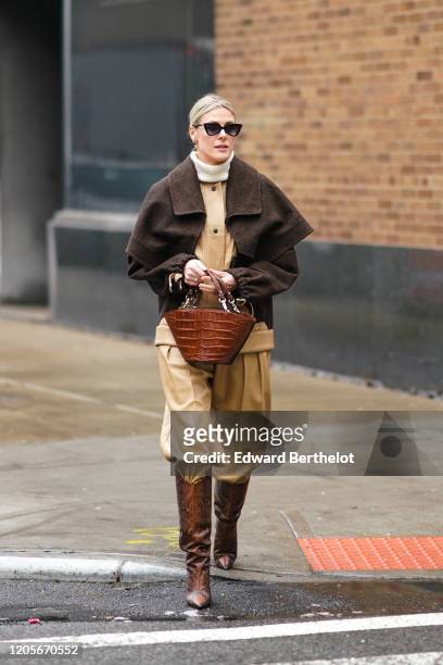 Sofie Valkiers wears sunglasses, a white turtleneck pullover, a brown jacket, a brown leather crocodile pattern bag, cream-color pants, brown leather...