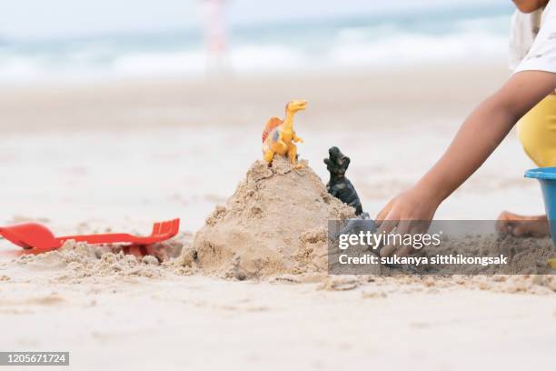 hands of little girl playing sand with miniature scale dinosaur on the beach near the sea. - dinosaur toy i - fotografias e filmes do acervo