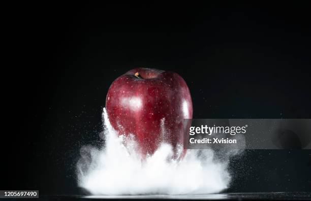 red apple flying in mid air with white flour sync. in high speed - frozen apple fotografías e imágenes de stock
