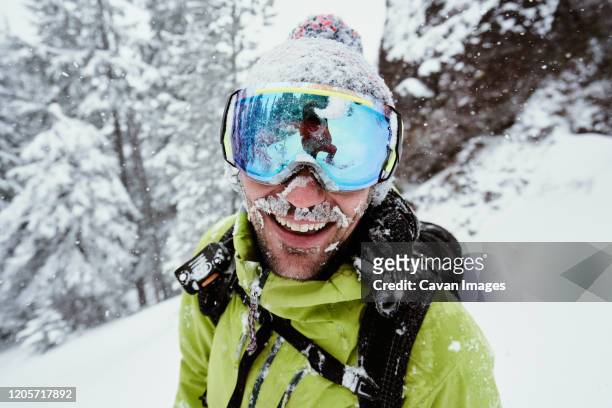 male snowboarder covered in snow smiling in winter - snow boarding stock-fotos und bilder