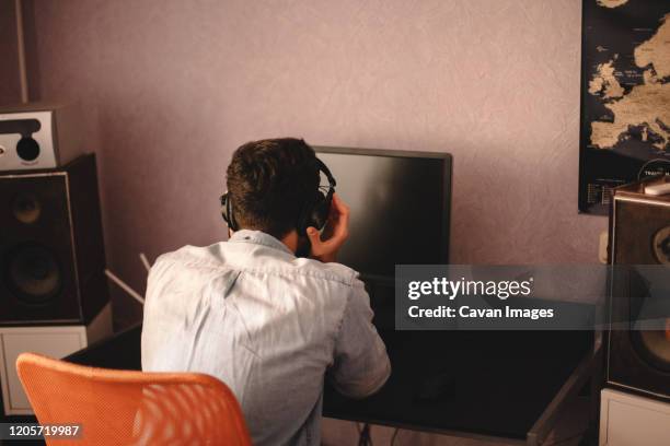 man holding headphones while listening music sitting by computer - top producer stock pictures, royalty-free photos & images