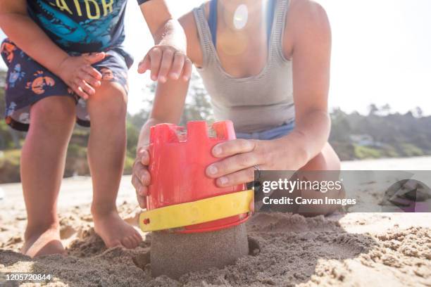 low angle of mother and son building sand castle. - zandkasteel stockfoto's en -beelden