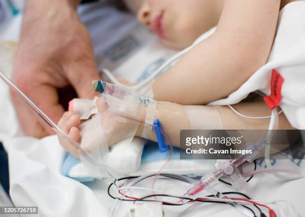 father holding hand of toddler in hospital hooked up to iv, pulse ox - child hospital stock-fotos und bilder