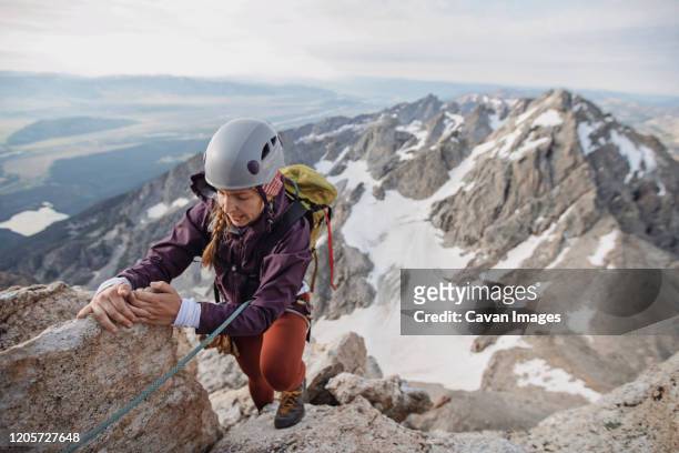female rock climber wearing helmet climbs a cliff in the tetons - messa in sicurezza foto e immagini stock