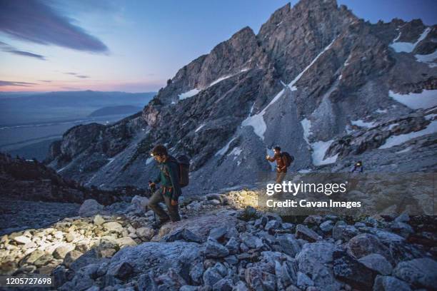 three hikers with lights walk along a trail in the tetons, sunrise - grand teton stock-fotos und bilder