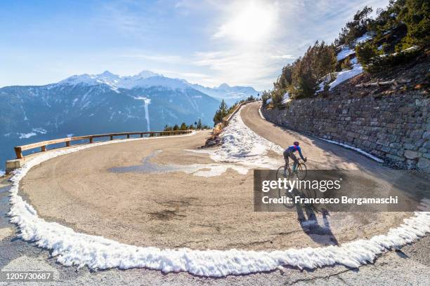 road cyclist climbing hairpin bends up mountain pass in winter with snow. - winter cycling ストックフォトと画像