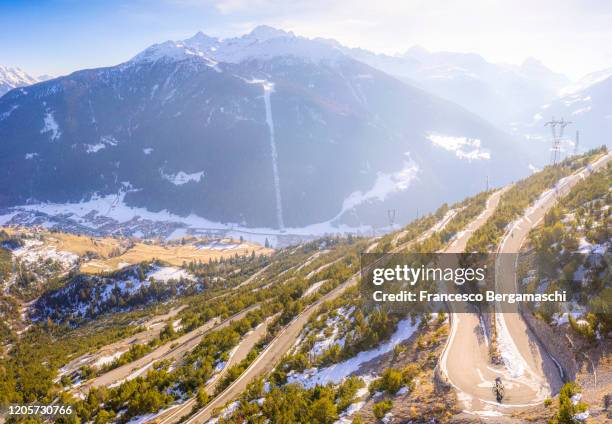 road cyclist climbing hairpin bends up mountain pass in winter with snow. - bormio stock pictures, royalty-free photos & images