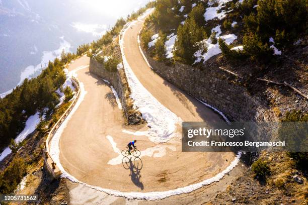 road cyclist climbing hairpin bends up mountain pass in winter with snow. - mountain biker stock-fotos und bilder