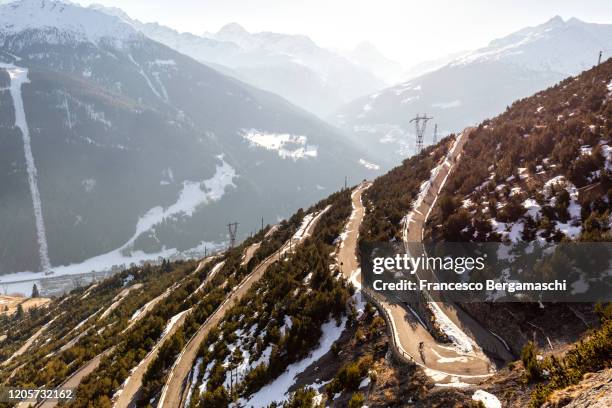 road cyclist climbing hairpin bends up mountain pass in winter with snow. - straßenradsport stock-fotos und bilder