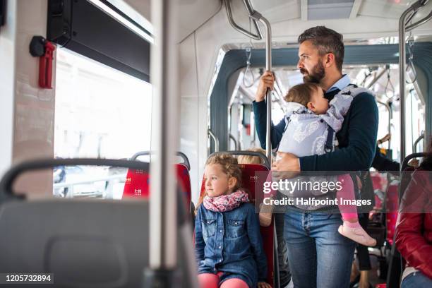 conscious father with daughter and toddler in carrier on bus in city, travelling. - leanincollection father fotografías e imágenes de stock