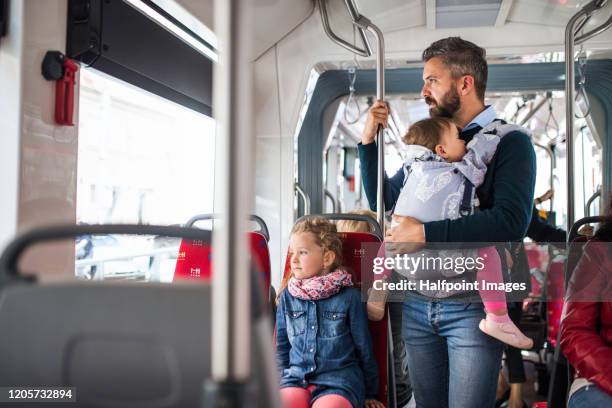 conscious father with daughter and toddler in carrier on bus in city, travelling. - leanincollection dad stock pictures, royalty-free photos & images