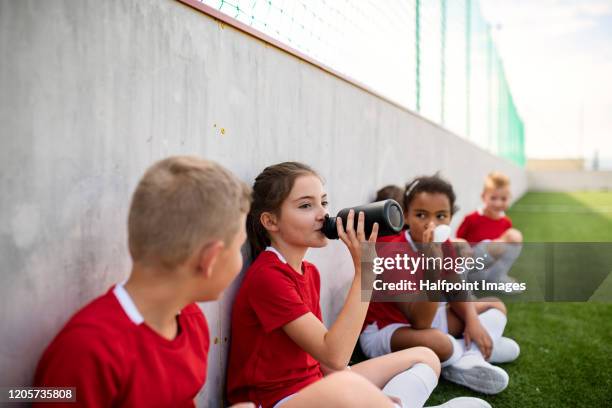 a group of children sitting outdoors on football pitch, resting. - club soccer photos et images de collection