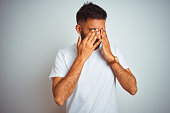 Young indian man wearing t-shirt standing over isolated white background rubbing eyes for fatigue and headache, sleepy and tired expression. Vision problem