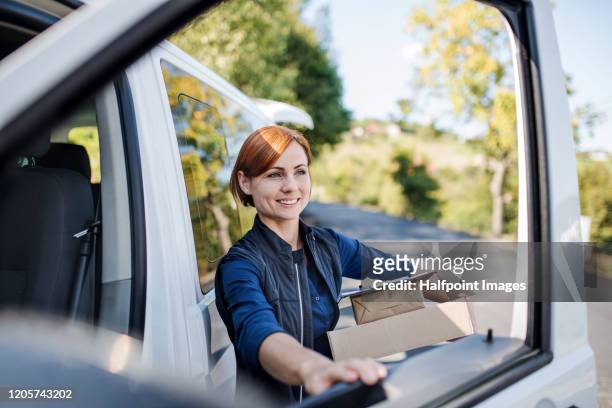 young woman courier by a delivery car, carrying parcels. - getting delivery stock-fotos und bilder