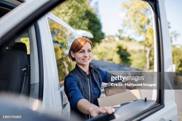 young woman courier by a delivery car, carrying parcels. - mensajero fotografías e imágenes de stock