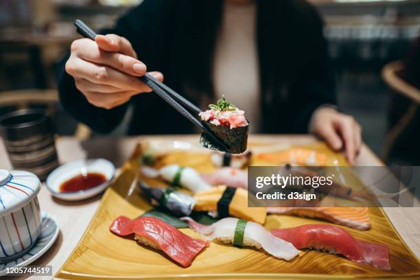 close up of young asian woman eating freshly made sushi with side dish and green tea in a japanese restaurant - comida japonesa fotografías e imágenes de stock