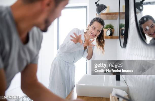 young couple standing indoors in bathroom at home, having fun when washing. - badezimmer mann stock-fotos und bilder