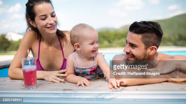 portrait of young couple with toddler girl in swimming pool outdoors at home. - babyschwimmen stock-fotos und bilder