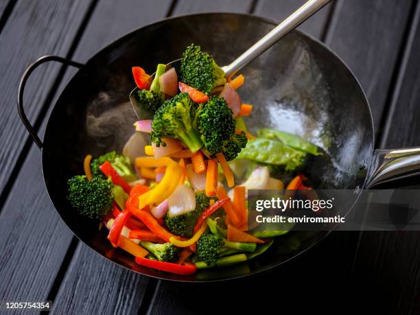 stir frying and sauteing a variety of fresh colorful market vegetables in a hot steaming wok. - salteado imagens e fotografias de stock