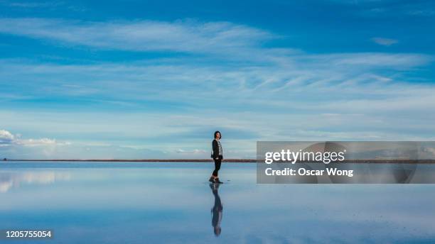 woman walking on salt flat against sky at salar de uyuni - salar de uyuni stockfoto's en -beelden